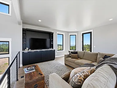 A wall-mounted television sits above dark cabinetry in a media nook beside a patterned sectional sofa at 2111 Vantage Circle.