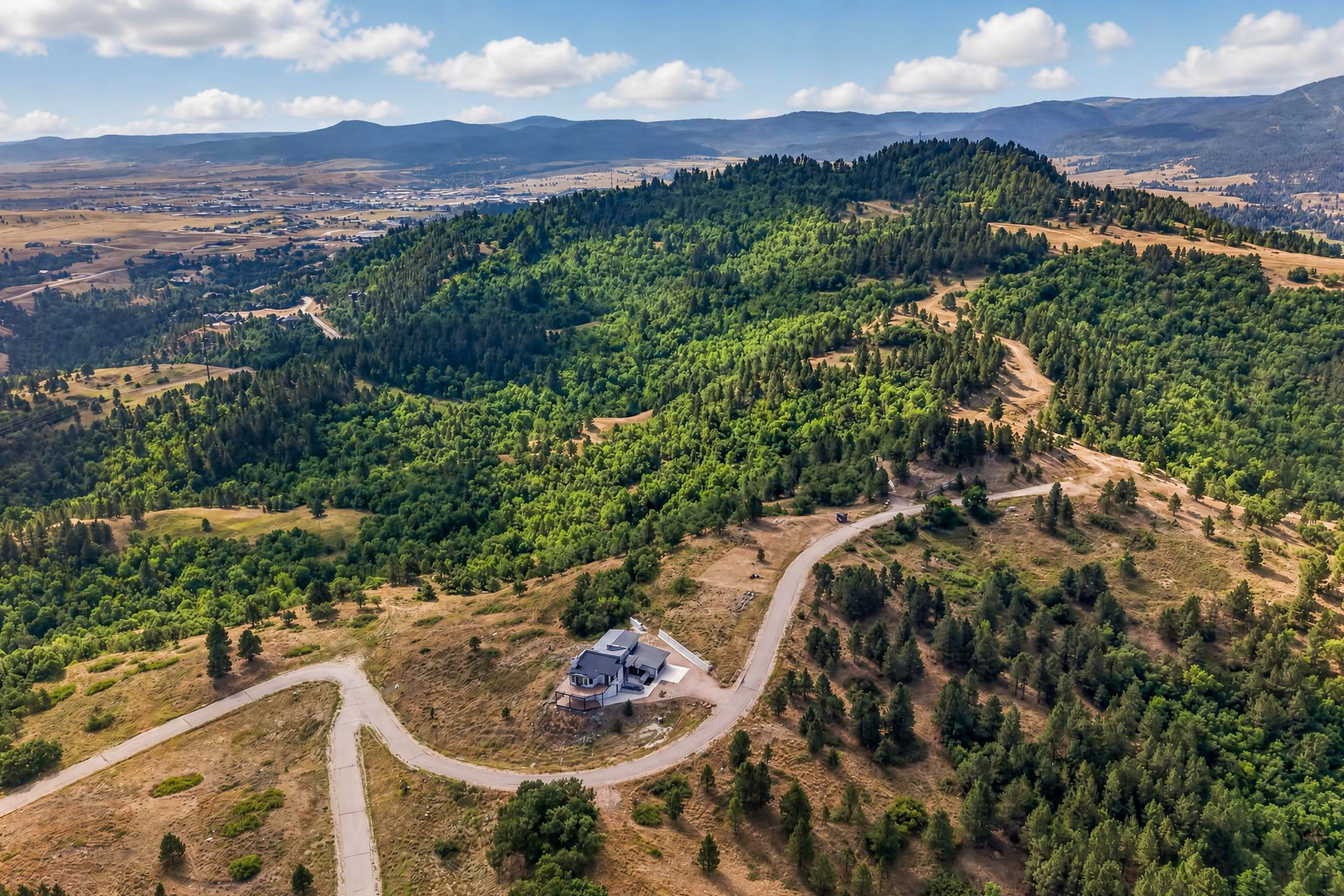An aerial view shows the home nestled among pine-covered hills