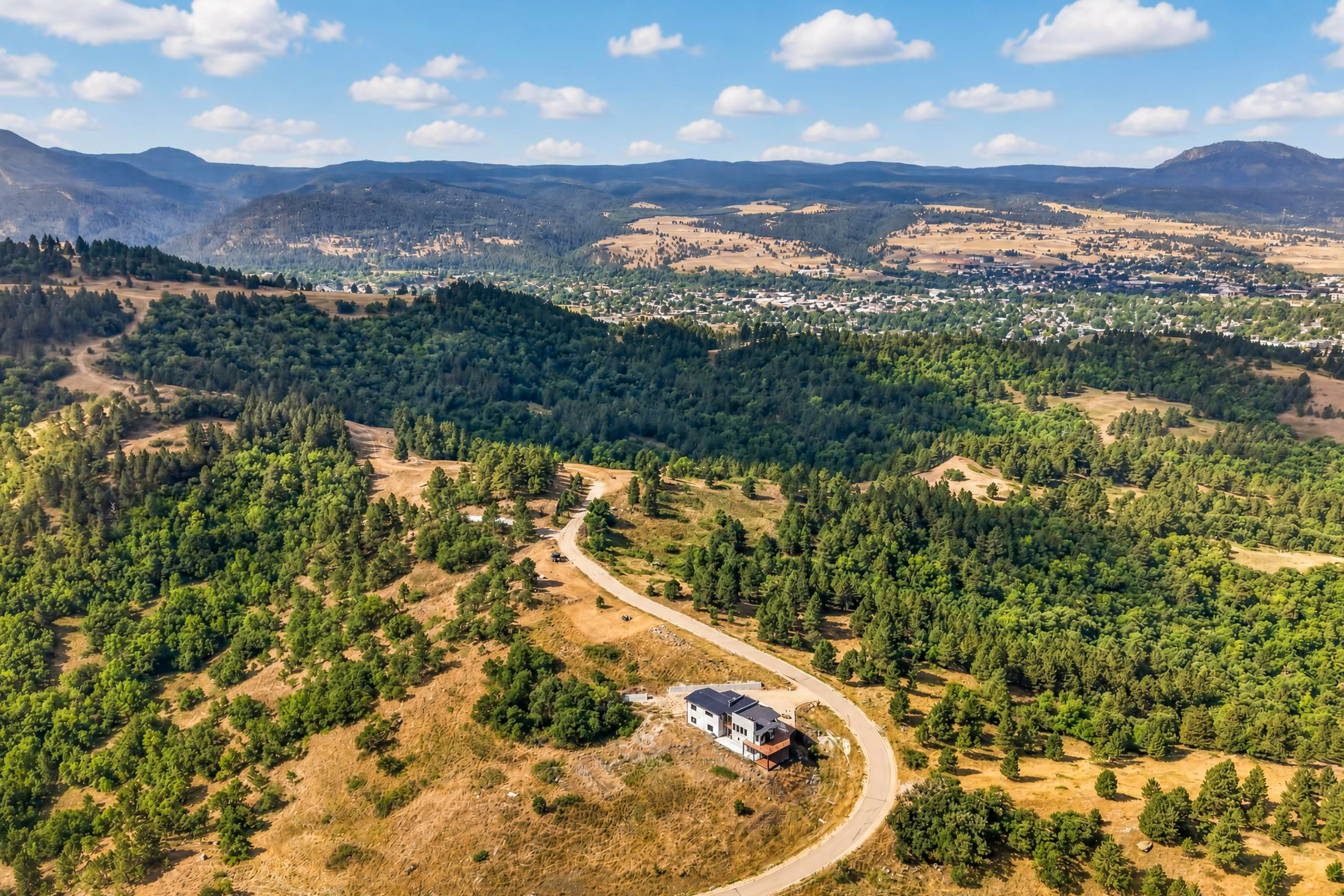 The property overlooks a forested valley with the town of Spearfish visible in the distance under a partly cloudy sky.