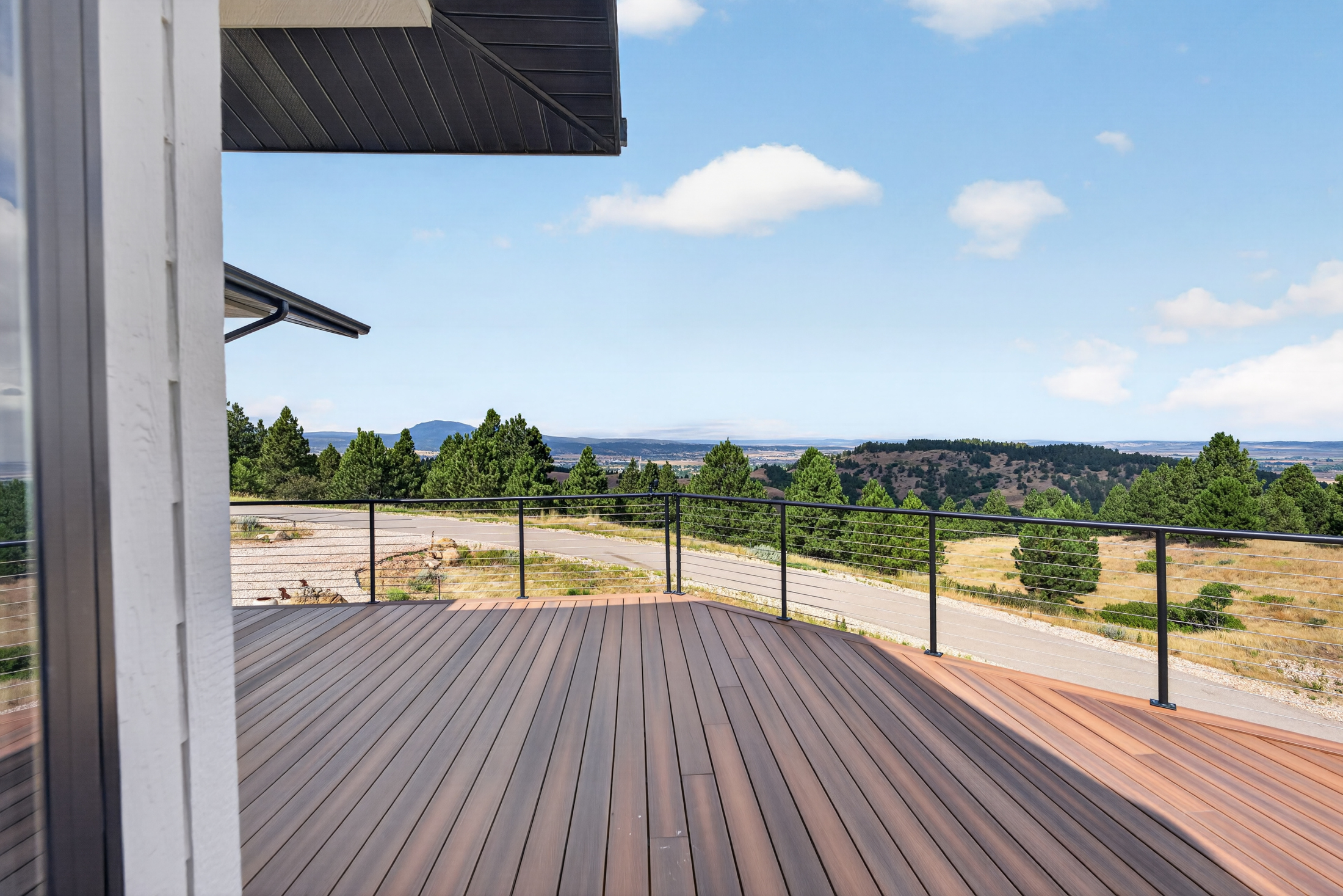 Composite decking leads to a black cable railing overlooking the driveway and surrounding grassland.