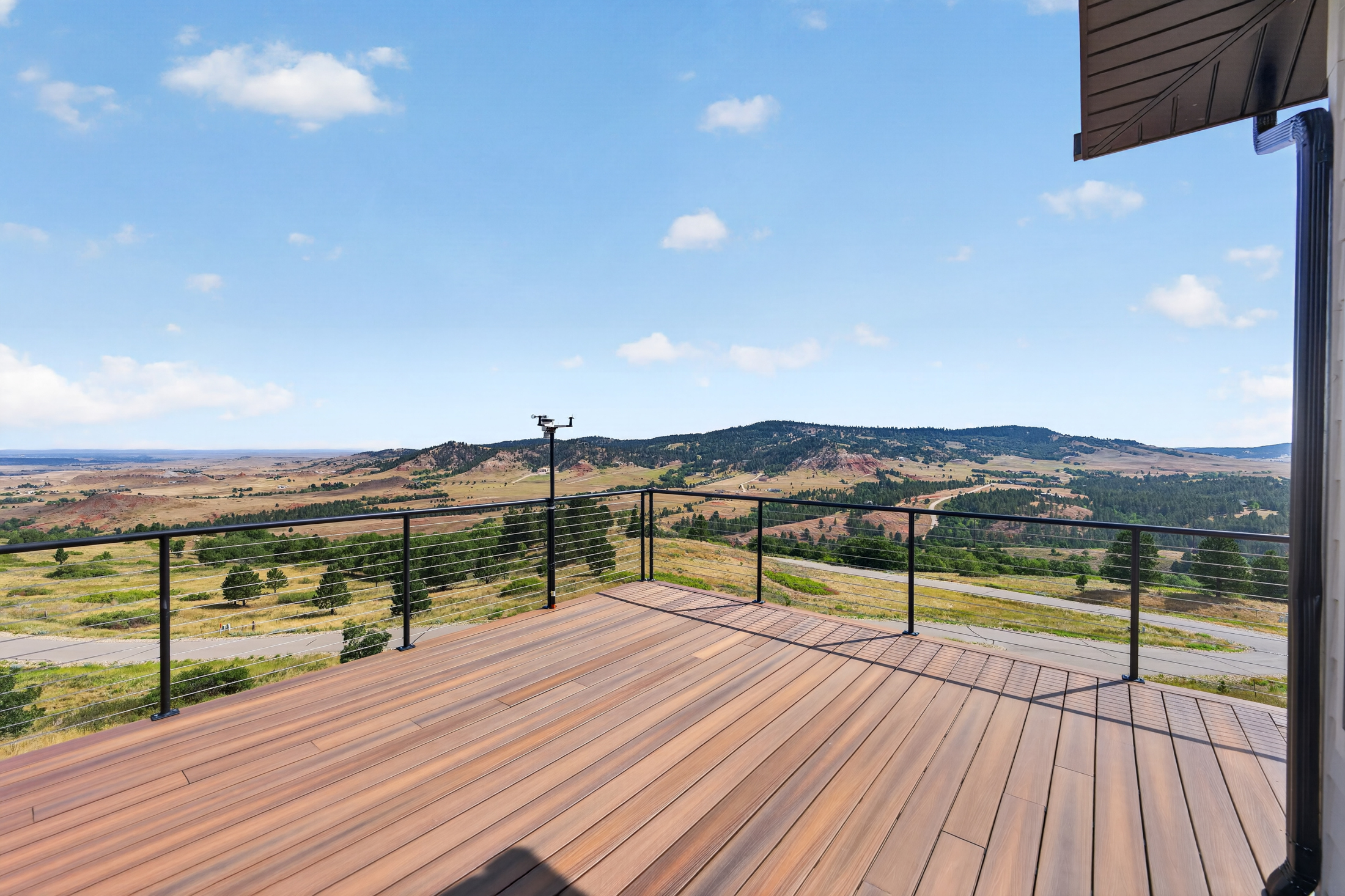 From the deck railing, rolling hills and open prairie stretch toward the horizon under a partly cloudy sky.