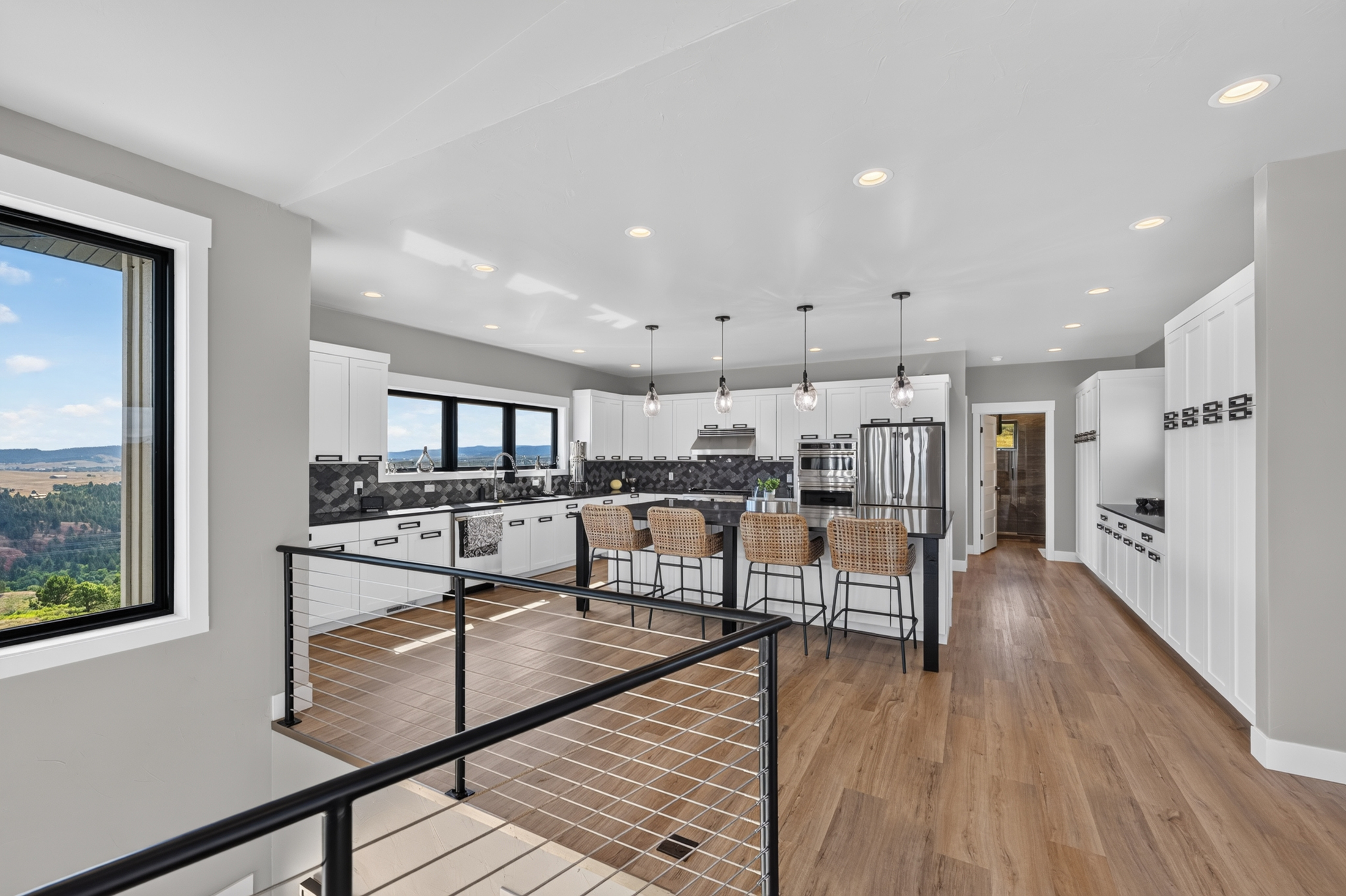 White cabinetry and a black-topped island with woven barstools sit beneath a window overlooking the Spearfish valley.