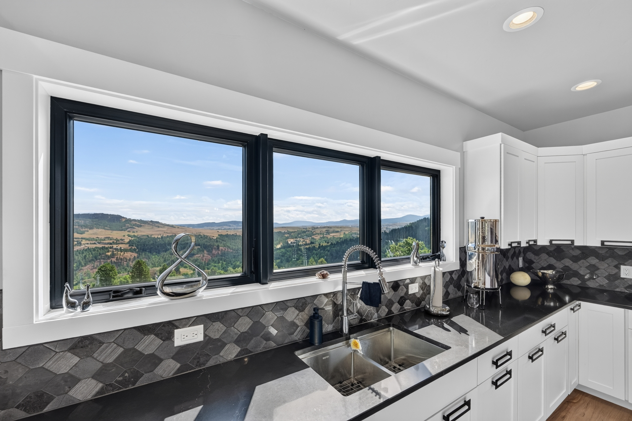 A stainless farmhouse-style sink looks out through a bank of windows onto forested hills and open valley at 2111 Vantage Circle.