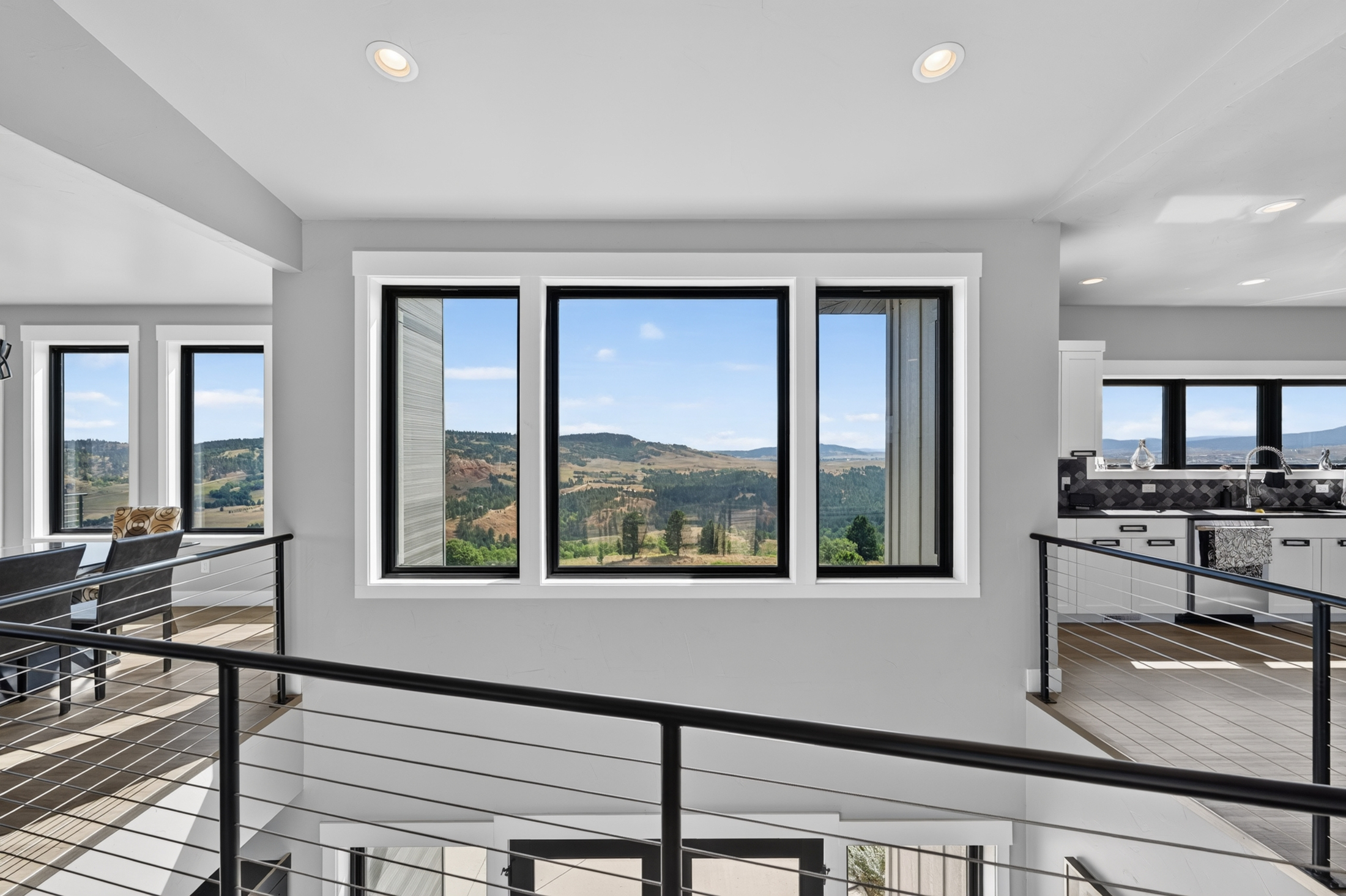 A wide window between the kitchen and dining area frames rolling hills and forest under a partly cloudy sky.
