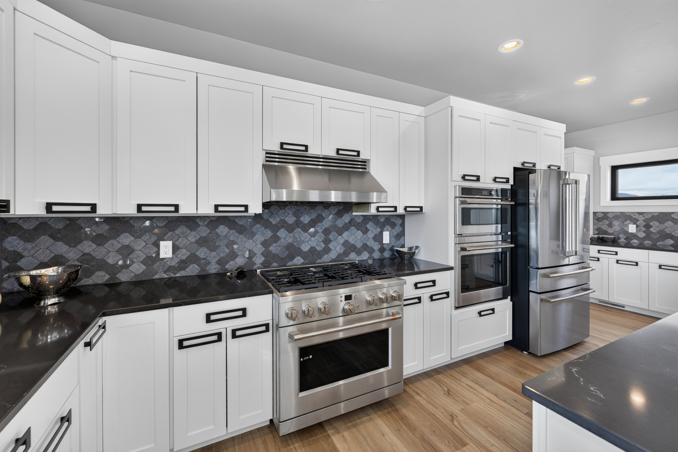 A stainless gas range sits beneath a vent hood, flanked by built-in double ovens and a refrigerator in the kitchen at 2111 Vantage Circle.